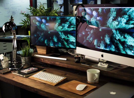 A busy desk with two computer monitors, a notebook and a MacBook