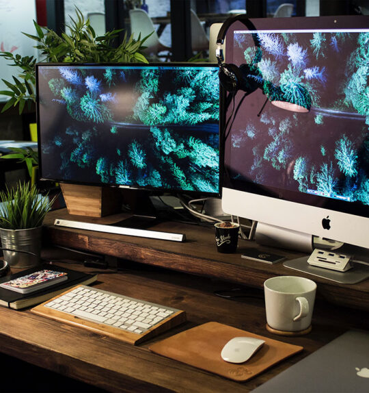 A busy desk with two computer monitors, a notebook and a MacBook