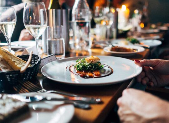 A person sitting over a gourmet meal at a long table with numerous plates and wine glasses
