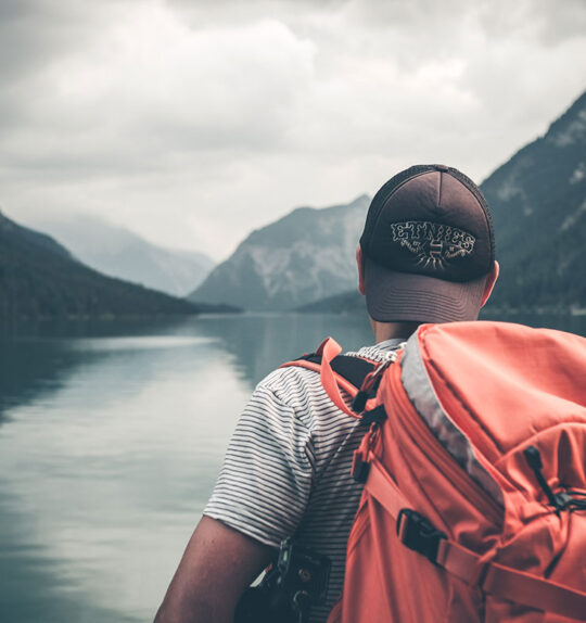 Hiker with a heavy backpack looking out at mountains and still water